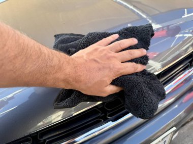 Araba yıkama yerinde siyah mikrofiber bezle el temizliği yapan bir adam var.