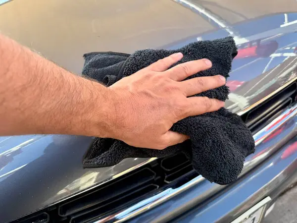 Araba yıkama yerinde siyah mikrofiber bezle el temizliği yapan bir adam var.