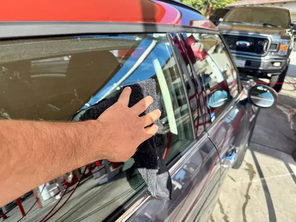 Araba yıkama yerinde siyah mikrofiber bezle el temizliği yapan bir adam var.