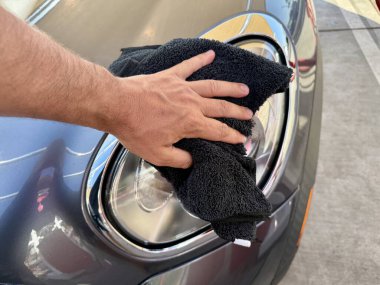 Araba yıkama yerinde siyah mikrofiber bezle el temizliği yapan bir adam var.