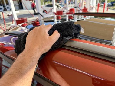 Araba yıkama yerinde siyah mikrofiber bezle el temizliği yapan bir adam var.