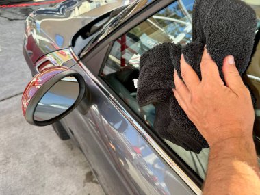 Araba yıkama yerinde siyah mikrofiber bezle el temizliği yapan bir adam var.