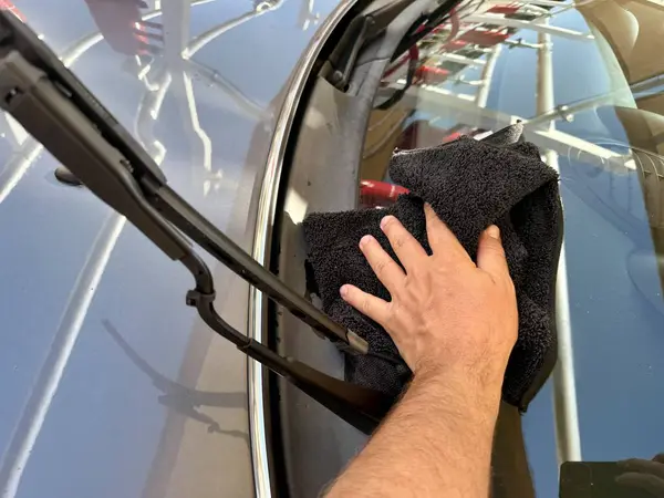 Araba yıkama yerinde siyah mikrofiber bezle el temizliği yapan bir adam var.