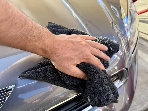 Araba yıkama yerinde siyah mikrofiber bezle el temizliği yapan bir adam var.