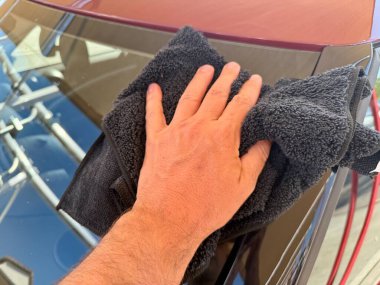 Araba yıkama yerinde siyah mikrofiber bezle el temizliği yapan bir adam var.