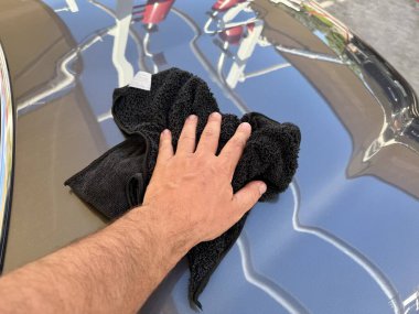Araba yıkama yerinde siyah mikrofiber bezle el temizliği yapan bir adam var.