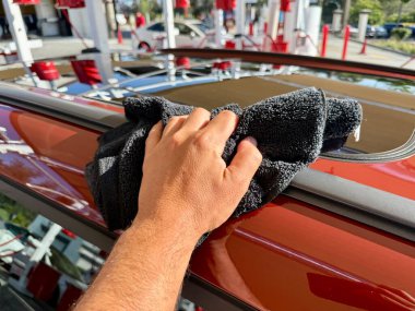 Araba yıkama yerinde siyah mikrofiber bezle el temizliği yapan bir adam var.