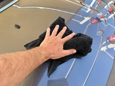 Araba yıkama yerinde siyah mikrofiber bezle el temizliği yapan bir adam var.