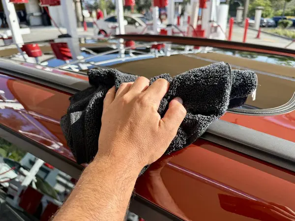 Araba yıkama yerinde siyah mikrofiber bezle el temizliği yapan bir adam var.