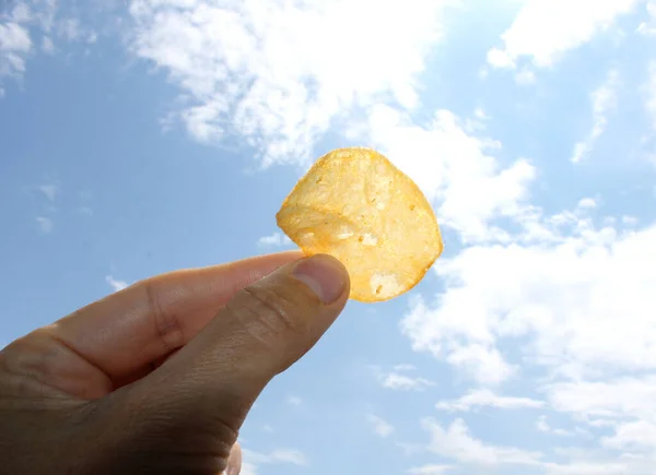 空を背景にポテトチップスを持って手を握る 不健康な食の概念 — ストック写真