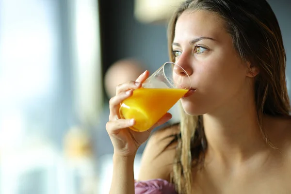 Młoda Kobieta Pije Sok Pomarańczowy Patrząc Przez Okno — Zdjęcie stockowe