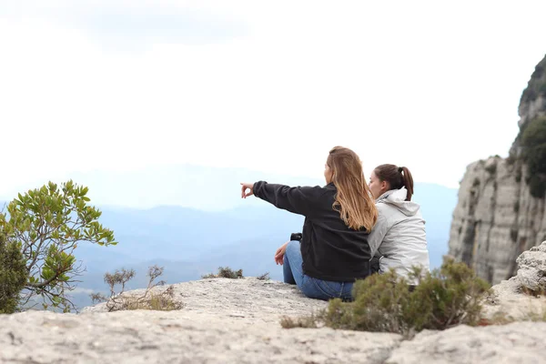 两个徒步旅行者坐在悬崖上凝视着大自然 指指点点 — 图库照片