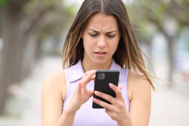 Endişeli bir gencin ön manzara portresi. Sokakta yürürken akıllı telefon içeriğini kontrol ediyor.