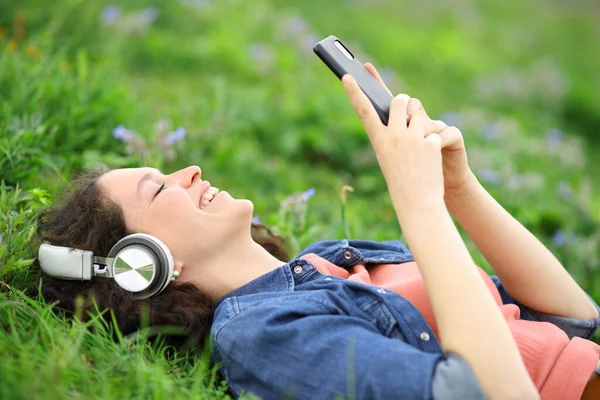 Parktaki Çimlerin Üzerinde Duran Kulaklıkla Telefonuyla Dinleyen Mutlu Bir Kadın — Stok fotoğraf
