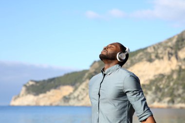 Rahat siyahi adam, plajda bir rehberi dinlerken kablosuz kulaklıkla meditasyon yapıyor.