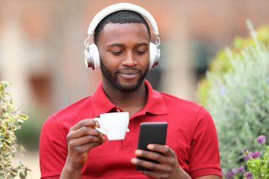 Ön manzara portresi, bir barda telefonla müzik dinleyen, kulaklık takan tatmin olmuş siyahi bir adam.