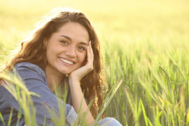 Buğday tarlasında kameraya gülümseyen mutlu güzel kadın.