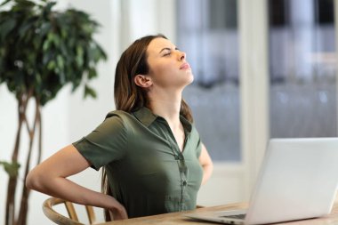 Dizüstü bilgisayarı olan bir kadın rahatsız bir sandalyede otururken sırt ağrısı çekiyor.