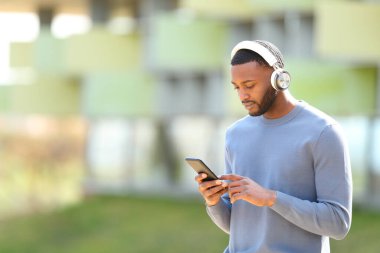 Zenci adam sokakta yürürken akıllı telefondan müziği kontrol ediyor.