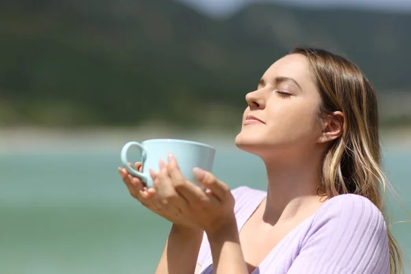 Woman in nature smelling coffee mug and relaxing