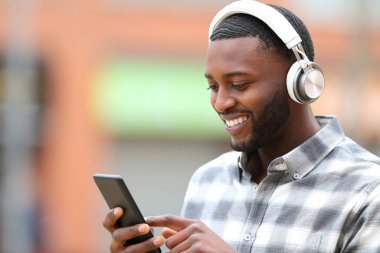 Black man listening to music checking phone outdoors in the street