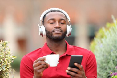 Black man relaxing and breathing listening to music with headphones and phone in a bar