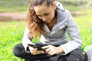 Hiker checking cell phone sitting on grass in nature