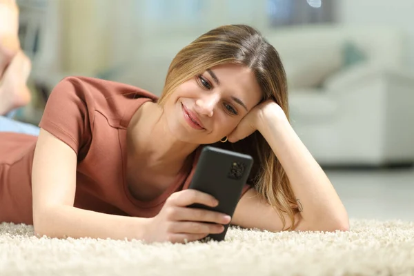 家でカーペットの上に横たわる女性のチェック電話 — ストック写真