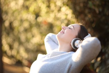 Parktaki bir bankta kulaklıkla müzik dinleyen mutlu bir kadının profili.