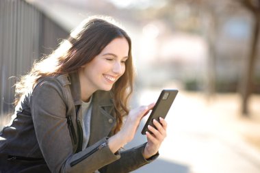 Güneşli bir günde sokakta cep telefonu kullanan mutlu bir kadın.