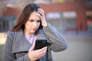 Endişeli kadın, kışın sokakta akıllı telefon içeriğini kontrol ediyor.