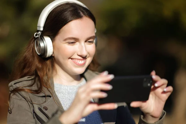 公園でヘッドフォンの視聴や携帯電話でビデオを聞いて幸せな女性 — ストック写真