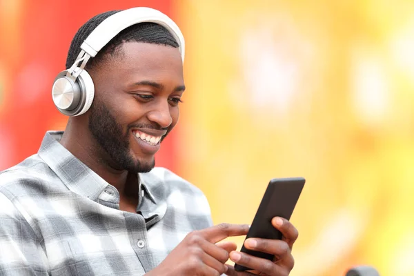 stock image Happy black man wearing headphones listening to music on smartphone