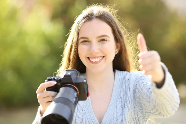 フロントビューポートレートの幸せな写真家保持ミラーレスカメラジェスチャー親指アップで公園 — ストック写真