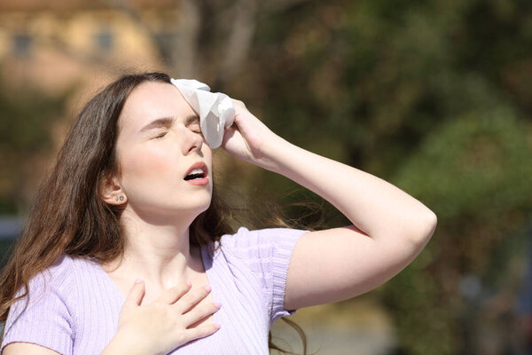 Stressed woman sweating and drying with a tissue in a park in summer