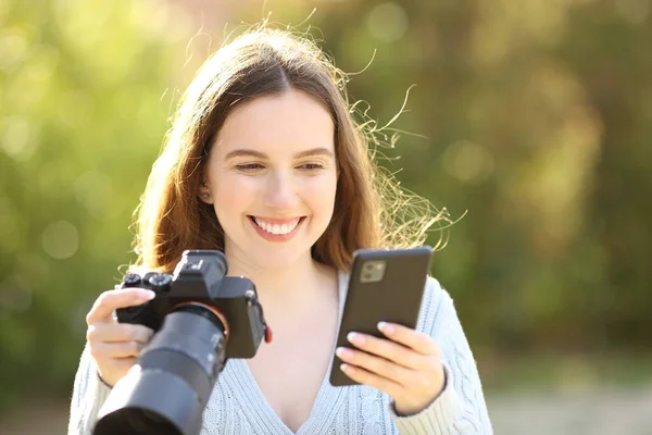 Fotógrafo Feliz Verificando Telefone Segurando Câmera Sem Espelho Parque — Fotografia de Stock