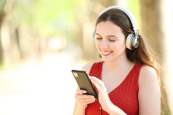 公園でスマートフォンスタンドを使用して音楽を聞いてヘッドフォンを身に着けて幸せな女性 — ストック写真