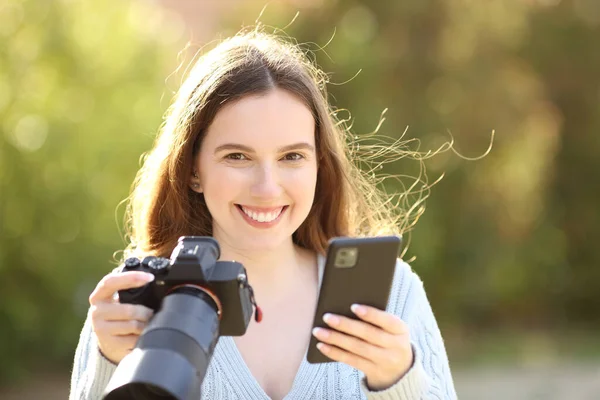 幸せな写真家はあなたが公園で携帯電話やミラーレスカメラを保持見て — ストック写真