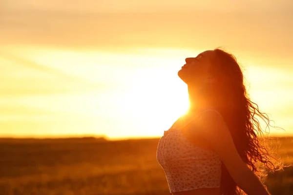 Profile of a female silhouette breathing fresh air at sunset in a field