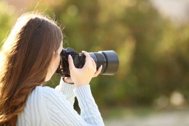 Bir fotoğrafçının arka plan portresi. Parkta aynasız fotoğraf makinesi ile fotoğraf çekiyor.