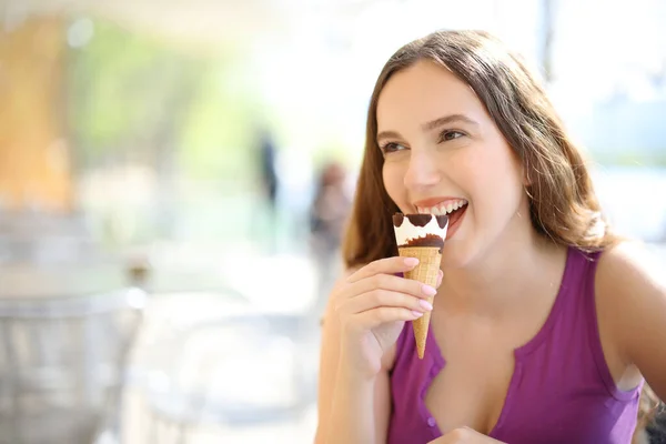 Happy woman eating ice cream in a restaurant terrace