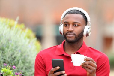 Kulaklıktan müzik dinleyen siyahi bir adamın portresi. Barda içki içerken başka yere bakıyor.