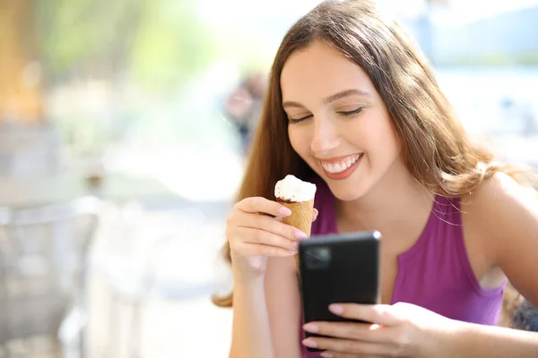 幸せな女性はアイスクリームを食べ バーのテラスに座って電話を使用して — ストック写真