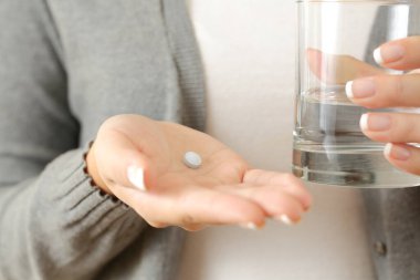 Ön tarafta elinde bir hap ve su bardağı olan bir kadının elleri var.