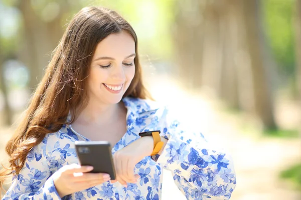 Szczęśliwa Kobieta Trzyma Telefon Sprawdzając Smartwatch Słonecznym Parku — Zdjęcie stockowe