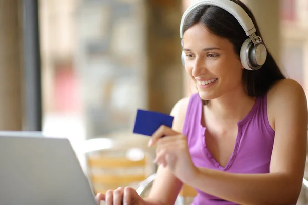 快乐的女人带着耳机 带着笔记本电脑和信用卡在咖啡店里购买在线Ppv媒体内容 — 图库照片