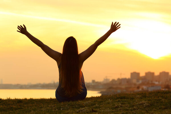 Back view portrait of a silhouette of a woman celebrating at sunset in outskirts