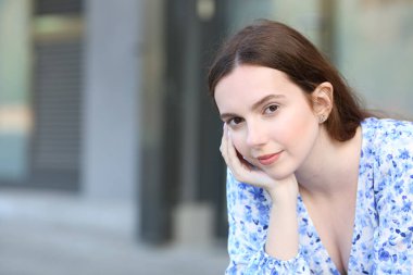 Kendine güvenen bir kadın sokakta oturan kameraya bakar.