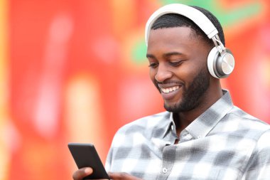 Mutlu siyah adam kırmızı arka planda kulaklık ve telefonla müzik dinliyor.