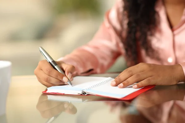Close up portrait of a black woman hands writing in agenda on a desk